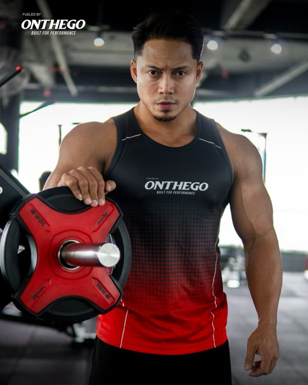 Person wearing a black and red athletic outfit with 'ONTHEGO' branding, holding a weight plate in a gym setting.
